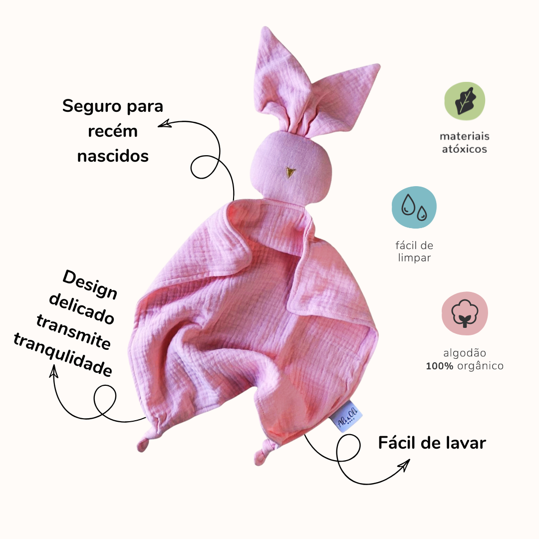Naninha de algodão em formato de coelho na cor rosa claro com informações sobre produtos. Do lado esquerdo da naninha as seguintes informações: Seguro para recém nascidos, design delicado, transmite tranquilidade. Do lado direito da naninha: materiais átoxicos, fácil de limpar, algodão 100% orgânico, fácil de lavar.