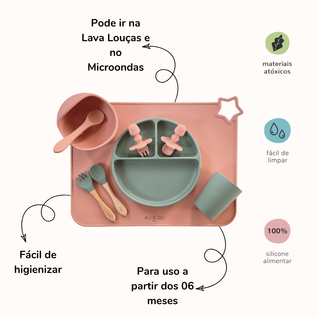 Imagem contem um Kit introdução alimentar bebê com um prato de silicone com tres divisorias sendo uma maior na horizontal e duas menores na vertical. Duas colheres pequenas para bebê de silicone com limitadores. Um jogo americano retangular com uma estrela no canto esquerdo superior e o escrito Ali & Oli Baby no centro inferior. Um bowl de silicone com ventosa e duas colheres com cabo de madeira de ponteiras de silicone, uma colher de silicone, e um copinho de silicone. As peças são umas rosa e outras verde