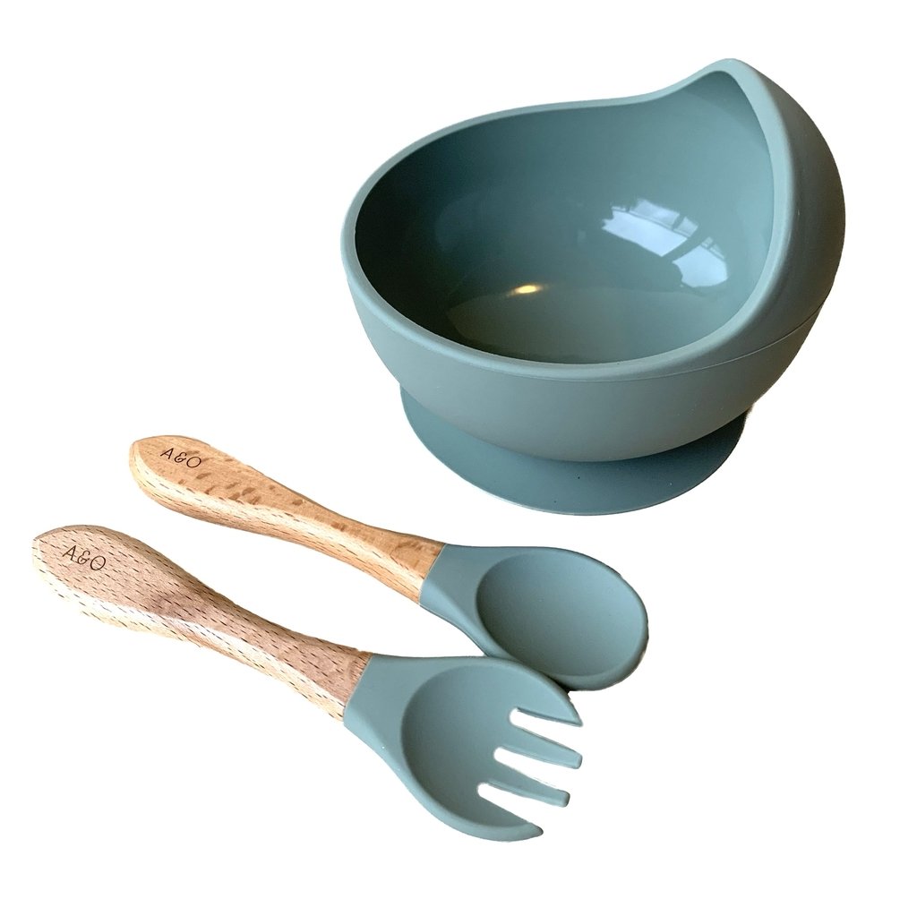 Um bowl de silicone com ventosa e duas colheres com cabo de madeira e ponteiras de silicone na cor verde sage.