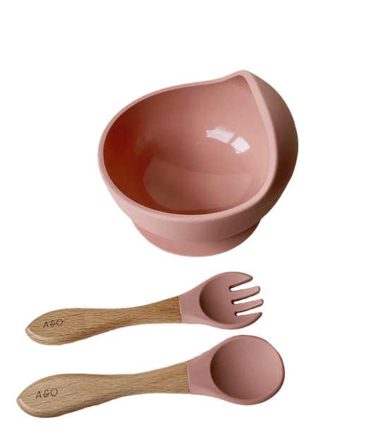 Um bowl com uma colher e um garfo com cabo de madeira e ponteira de silicone na cor rosa blush