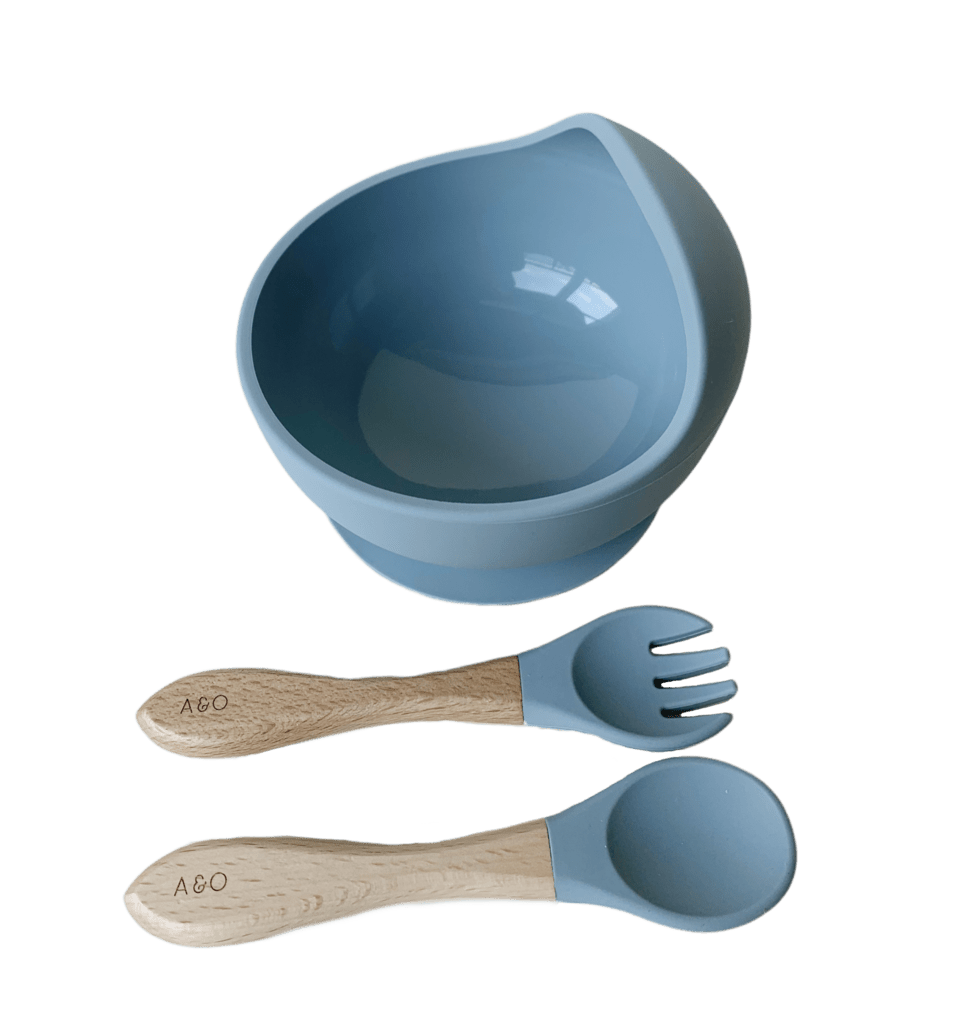 Um bowl com uma colher e um garfo com cabo de madeira e ponteira de silicone na cor azul ether.