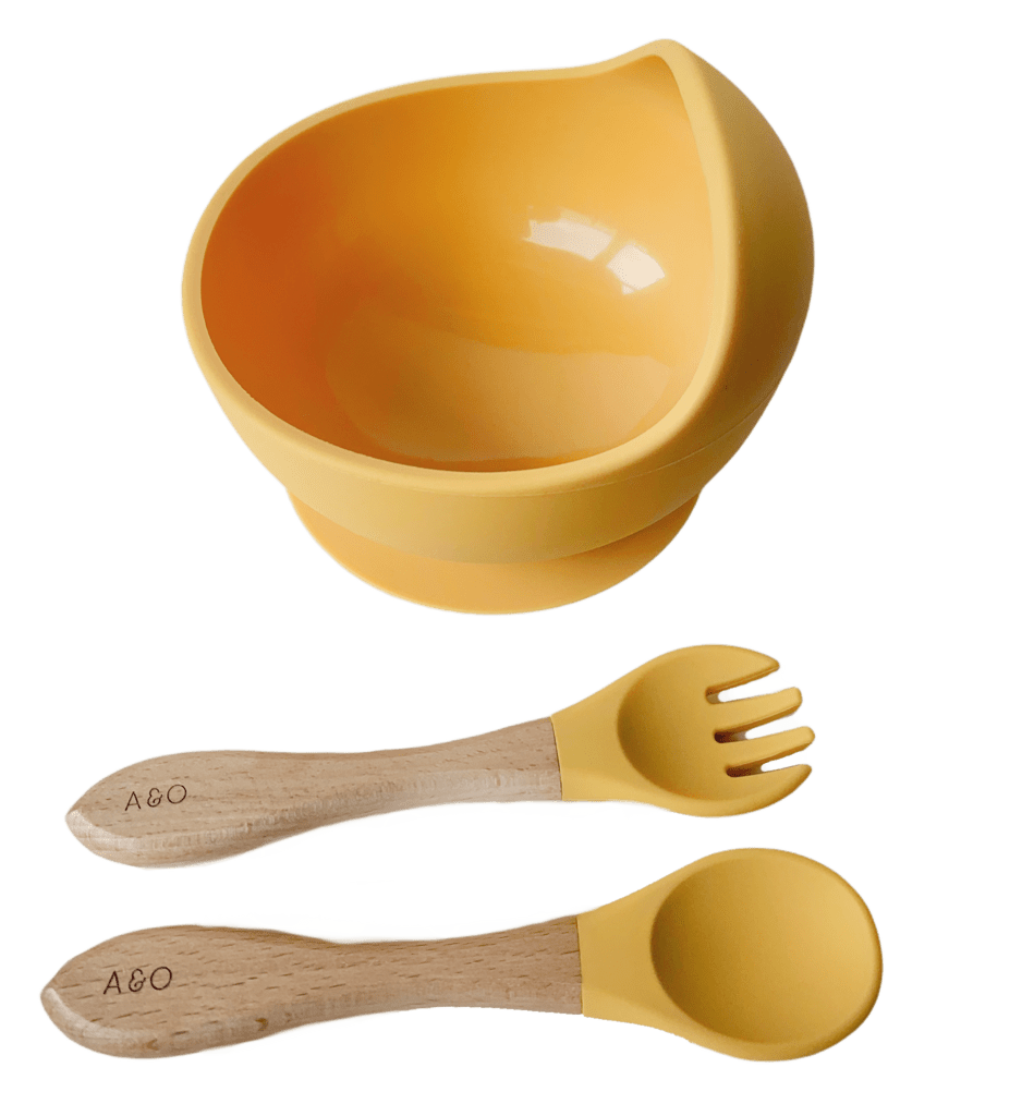 Um bowl com uma colher e um garfo com cabo de madeira e ponteira de silicone na cor amarelo mostarda.