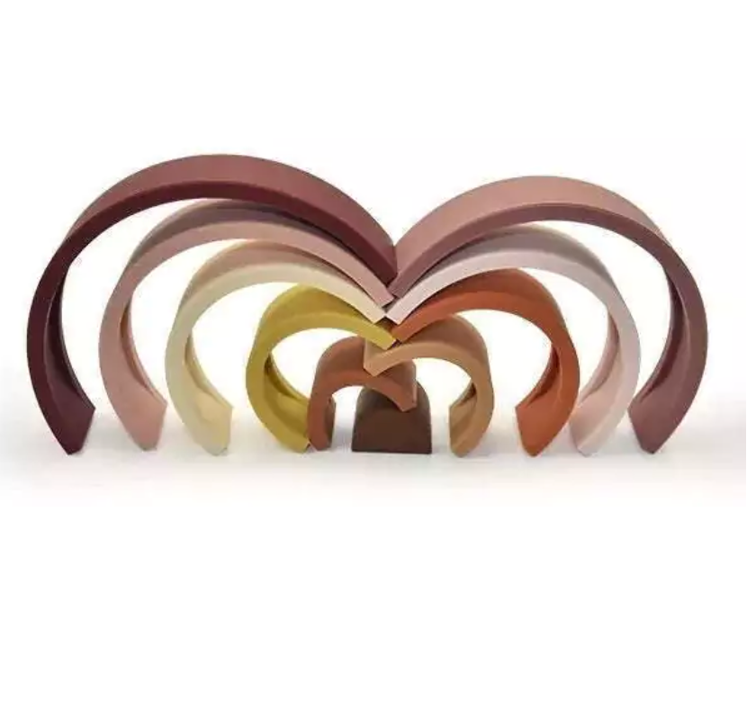 Arco-íris feito de tiras de silicone nas cores marrom, rosa, amarelo mostarda e laranja. Peças desmontáveis para brincar e empilhar e encaixar. Peças colocadas umas sobre as outras para ilustrar como podem ser colocadas