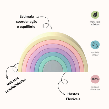 Arco-íris feito de tiras de silicone nas cores cinza, verde água, azul, roxo, lilás, laranja claro e amarelo claro. Peças desmontáveis para brincar e empilhar e encaixar. Imagem com informações sobre o produto. Do lado esquerdo do produto: Estimula coordenação e equilíbrio, infinitas possibilidades. Do lado direito do produto: materiais atóxicos, fácil de limpar, silicone alimentar e hastes flexíveis.