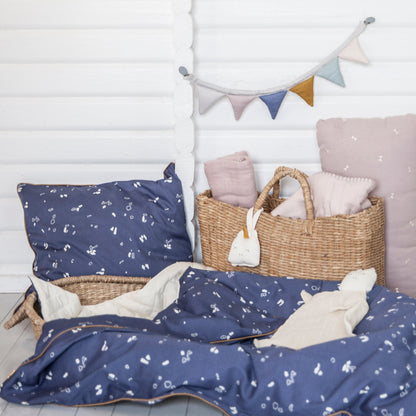 Imagem de uma quarto com uma cesta, com travesseiros na cor azul escuro, uma parede com bandeirinhas penduradas, uma colcha azul escuro no chão e uma naninha e na cesta, o chocalho em formato de unicornio esta pendurado.