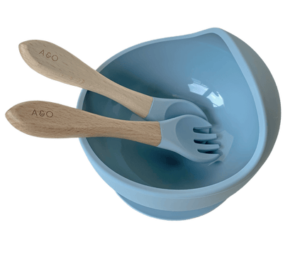 Um bowl de silicone com ventosa e duas colheres com cabo de madeira e ponteiras de silicone na cor azul ether.