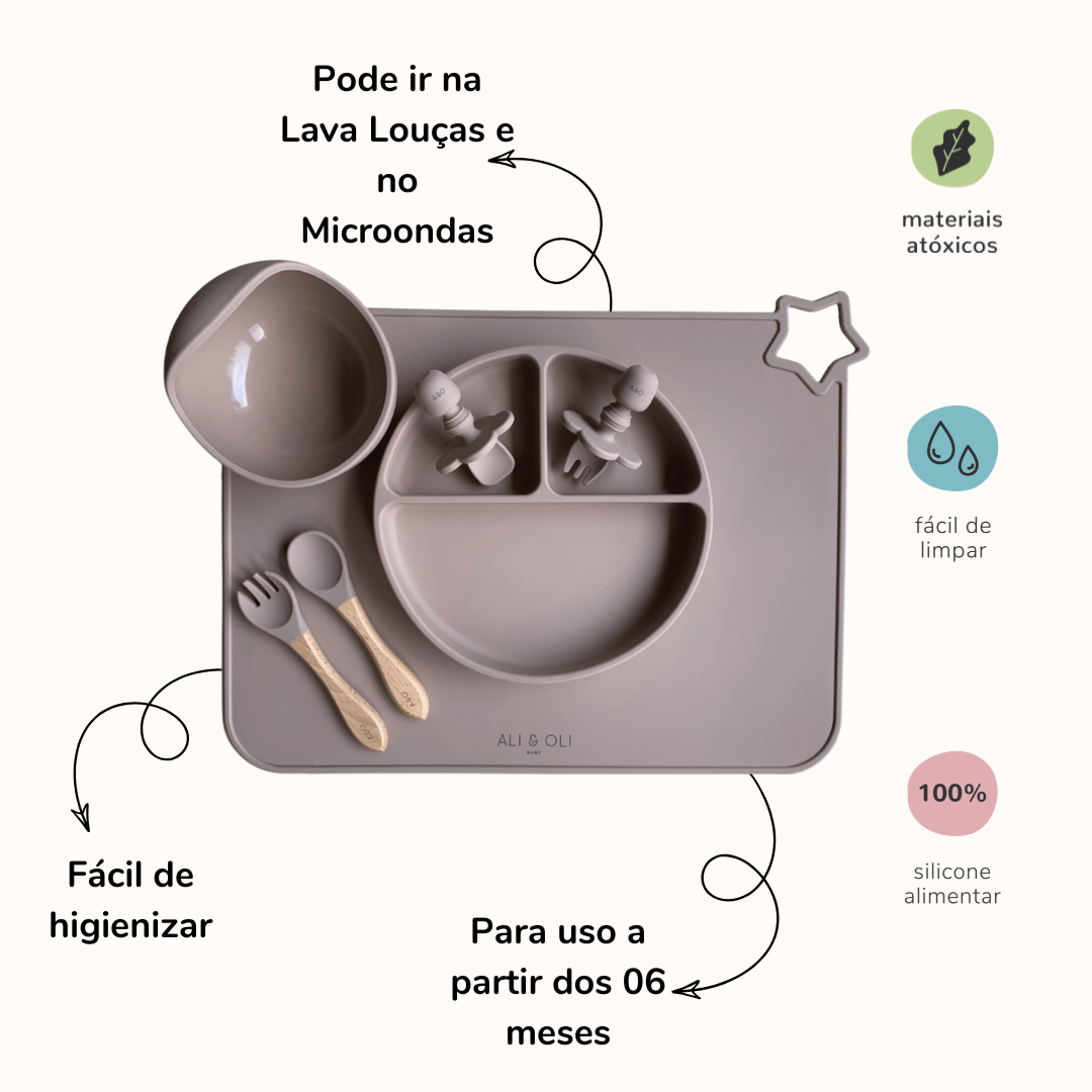 Imagem contem um Kit introdução alimentar bebê com um prato de silicone com tres divisorias sendo uma maior na horizontal e duas menores na vertical. Duas colheres pequenas para bebê de silicone com limitadores. Um jogo americano retangular com uma estrela no canto esquerdo superior e o escrito Ali & Oli Baby no centro inferior. Um bowl de silicone com ventosa e duas colheres com cabo de madeira de ponteiras de silicone. Todas as peças são na cor nude. Imagem contem descrição e informações sobre produto.