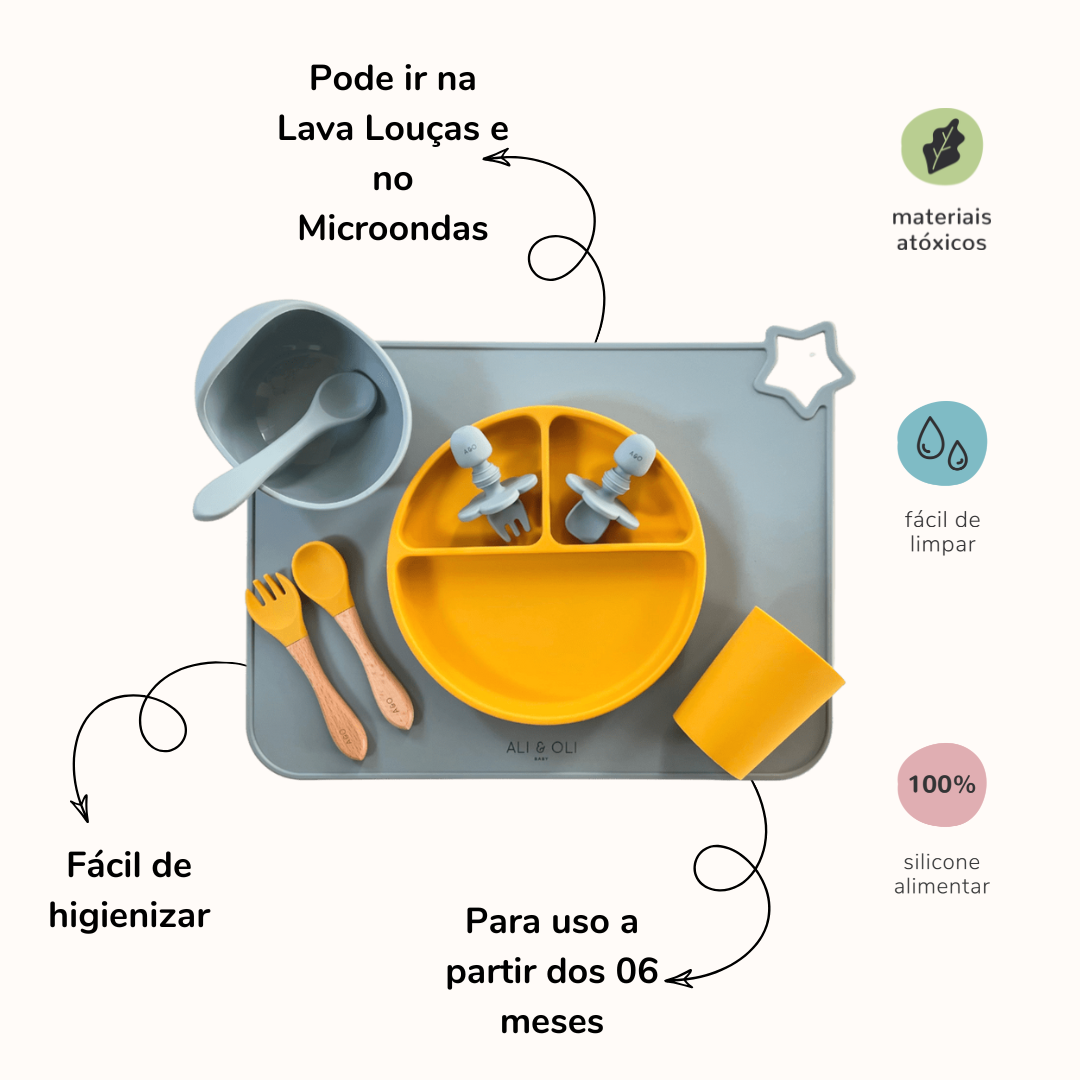 Imagem contem um Kit introdução alimentar bebê com um prato de silicone com tres divisorias sendo uma maior na horizontal e duas menores na vertical. Duas colheres pequenas para bebê de silicone com limitadores. Um jogo americano retangular com uma estrela no canto esquerdo superior e o escrito Ali & Oli Baby no centro inferior. Um bowl de silicone com ventosa e duas colheres com cabo de madeira de ponteiras de silicone, uma colher de silicone, e um copinho de silicone. As peças são umas azul e outras amare