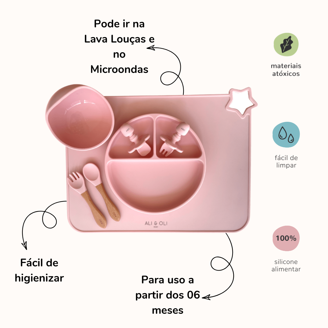 Imagem contem um Kit introdução alimentar bebê com um prato de silicone com tres divisorias sendo uma maior na horizontal e duas menores na vertical. Duas colheres pequenas para bebê de silicone com limitadores. Um jogo americano retangular com uma estrela no canto esquerdo superior e o escrito Ali & Oli Baby no centro inferior. Um bowl de silicone com ventosa e duas colheres com cabo de madeira de ponteiras de silicone. Todas as peças são na cor Rosa bebê. Imagem contem descrição de informações do produto