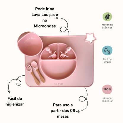 Imagem contem um Kit introdução alimentar bebê com um prato de silicone com tres divisorias sendo uma maior na horizontal e duas menores na vertical. Duas colheres pequenas para bebê de silicone com limitadores. Um jogo americano retangular com uma estrela no canto esquerdo superior e o escrito Ali & Oli Baby no centro inferior. Um bowl de silicone com ventosa e duas colheres com cabo de madeira de ponteiras de silicone. Todas as peças são na cor Rosa bebê. Imagem contem descrição de informações do produto