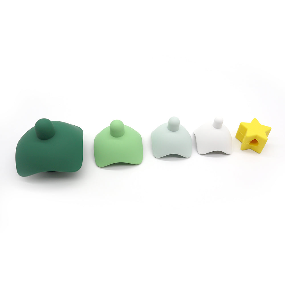 Árvore de natal em formato de peças de silicone encaixadas uma sobre a outras nas cores verde escuro, verde claro, cinza, branco e por ultimo uma estrela amarela. As peças estão desmontadas e enfileiradas de direitas para esquerda na ordem de cores
